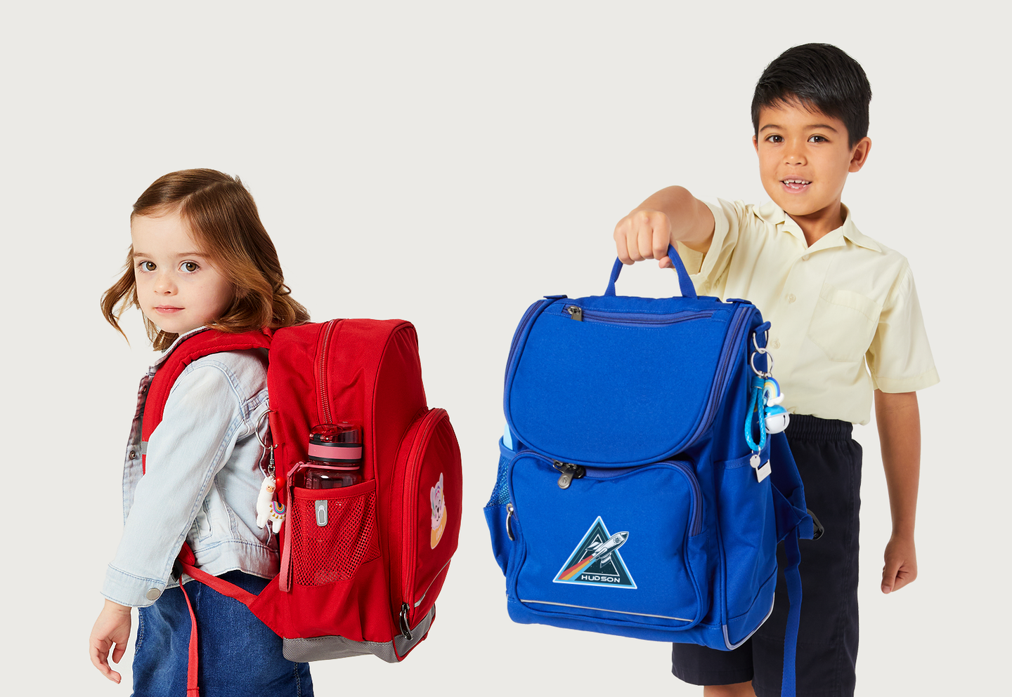 Three year old girl wearing a red Harlequin Kindy Backpack and a seven year old boy holding a Royal Blue Harlequin Mighty Backpack.
