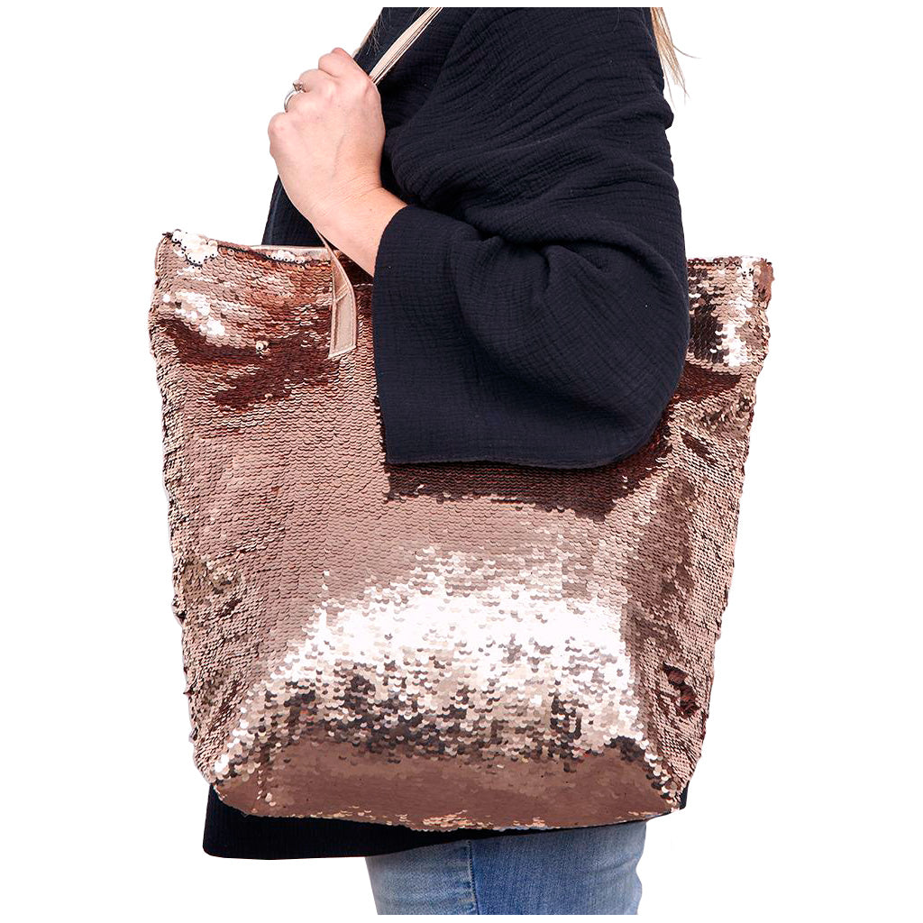 Person holding the Better Tote rose gold sequence bag with long over the shoulder carry handle, with reversible rose gold sequins covering the whole front of the bag
