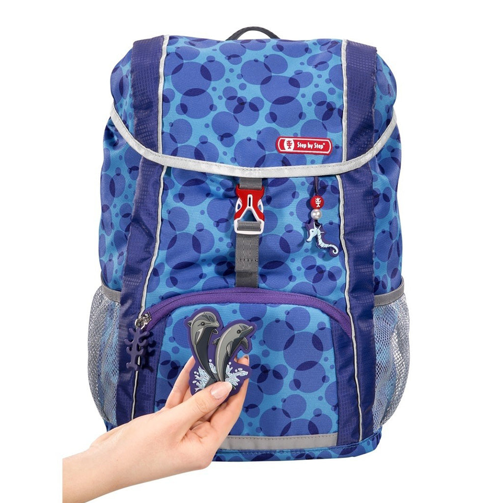 Blue and Purple dot Step By Step Junior Happy Dolphin backpack front angle view displaying a top pocket, a buckle clip and a seahorse chain with a front lower pocket at the bottom, two side water bottle holders, showcasing the magnetic dolphin