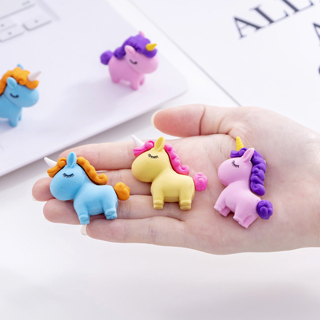A set of three small chunky unicorn erasers in pink, blue and yellow shown resting on a small women's hand