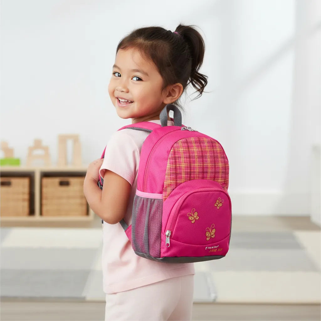 Child wearing a pink backpack with plaid pattern and butterflies on the pocket, she is standing looking after her shoulders indoors