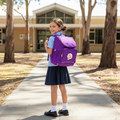 Young girl in a school uniform with a purple Harlequin Kids backpack standing on a school pathway.