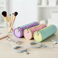 Pastel-colored cylindrical pouches on a desk with makeup brushes and scissors.